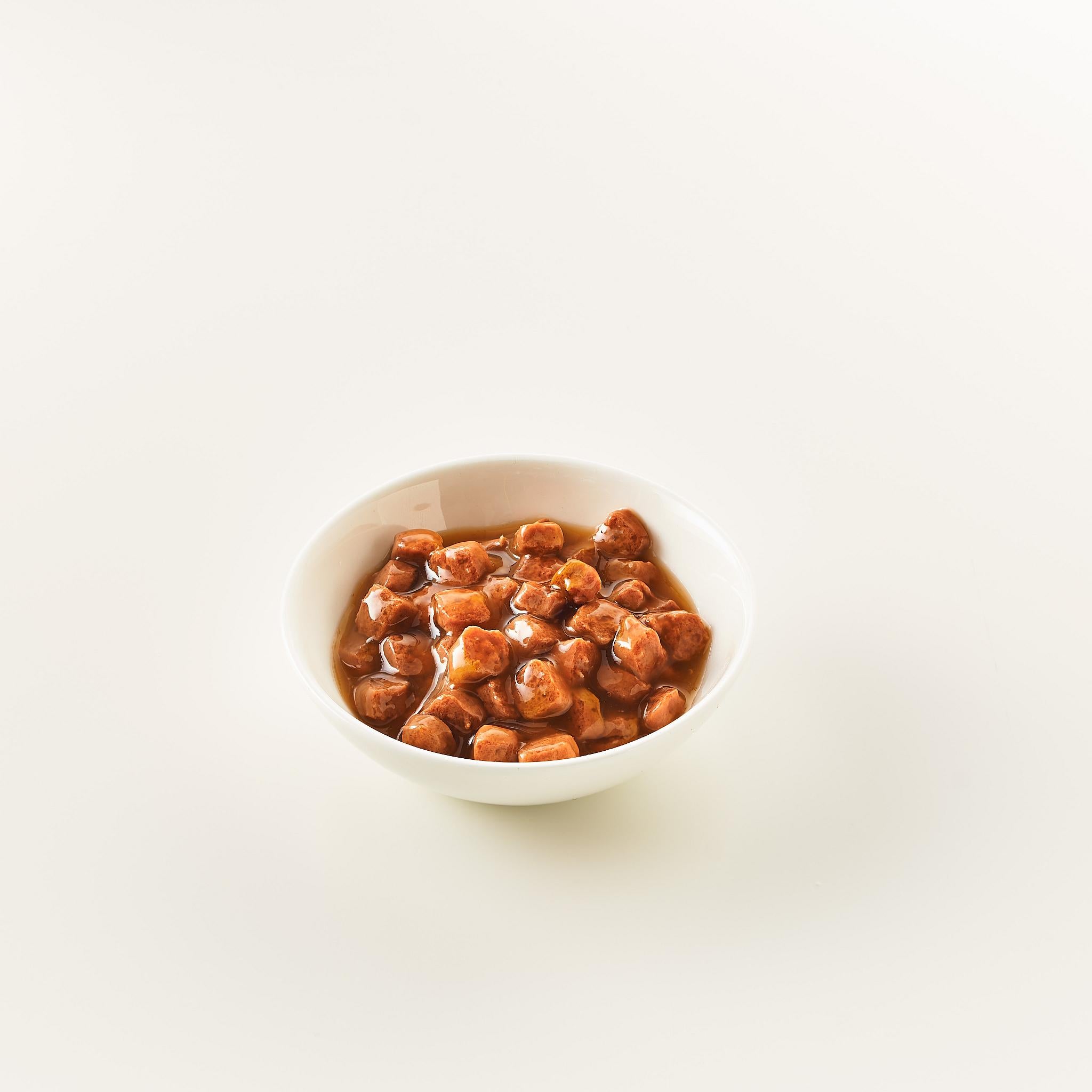 Eine weiße Schüssel mit braunen Würfeln in einer dunklen Sauce.