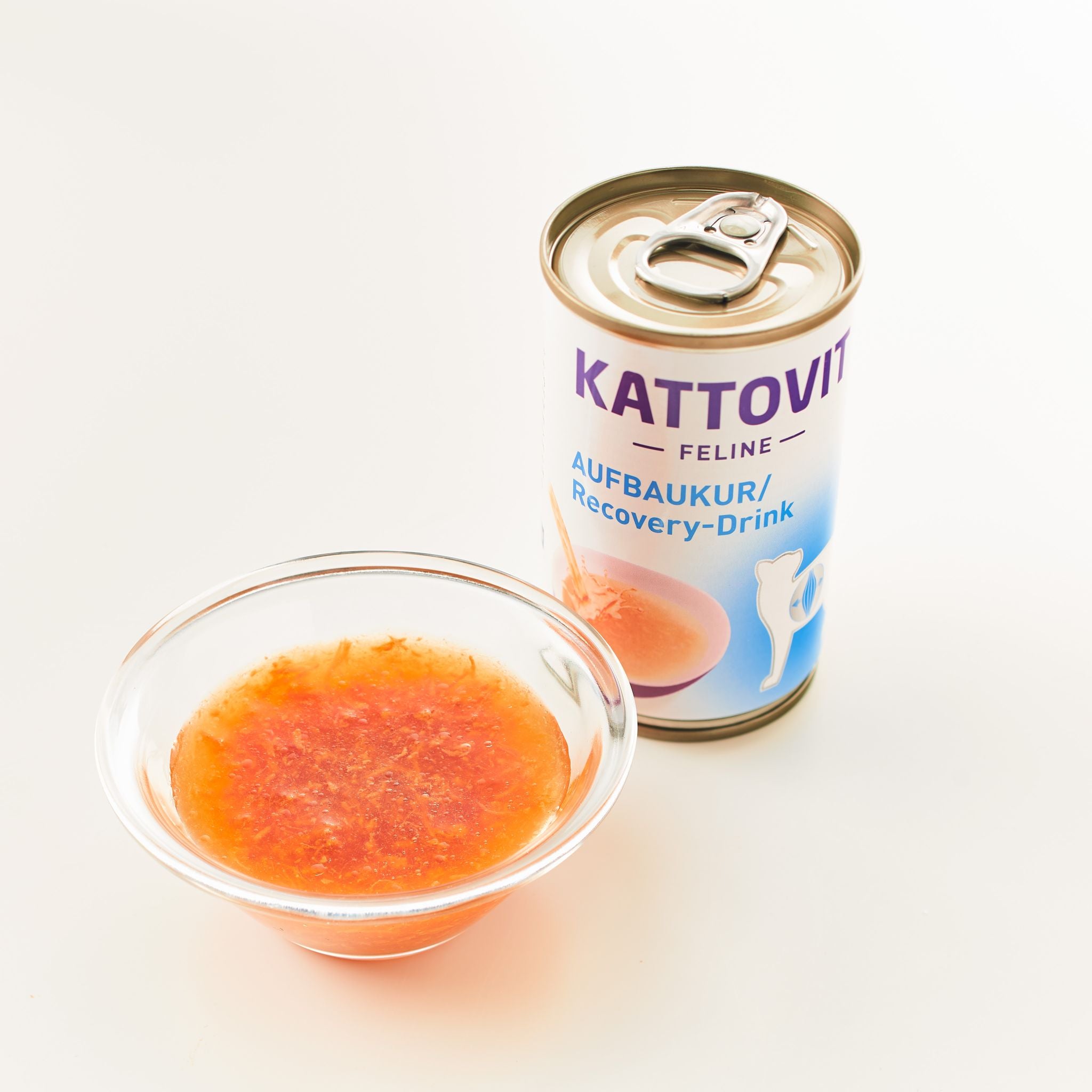 Ein Glasgefäß mit einer orangefarbenen Flüssigkeit vor einer Verpackung eines Aufbaukur-Drinks von KATTOVIT.