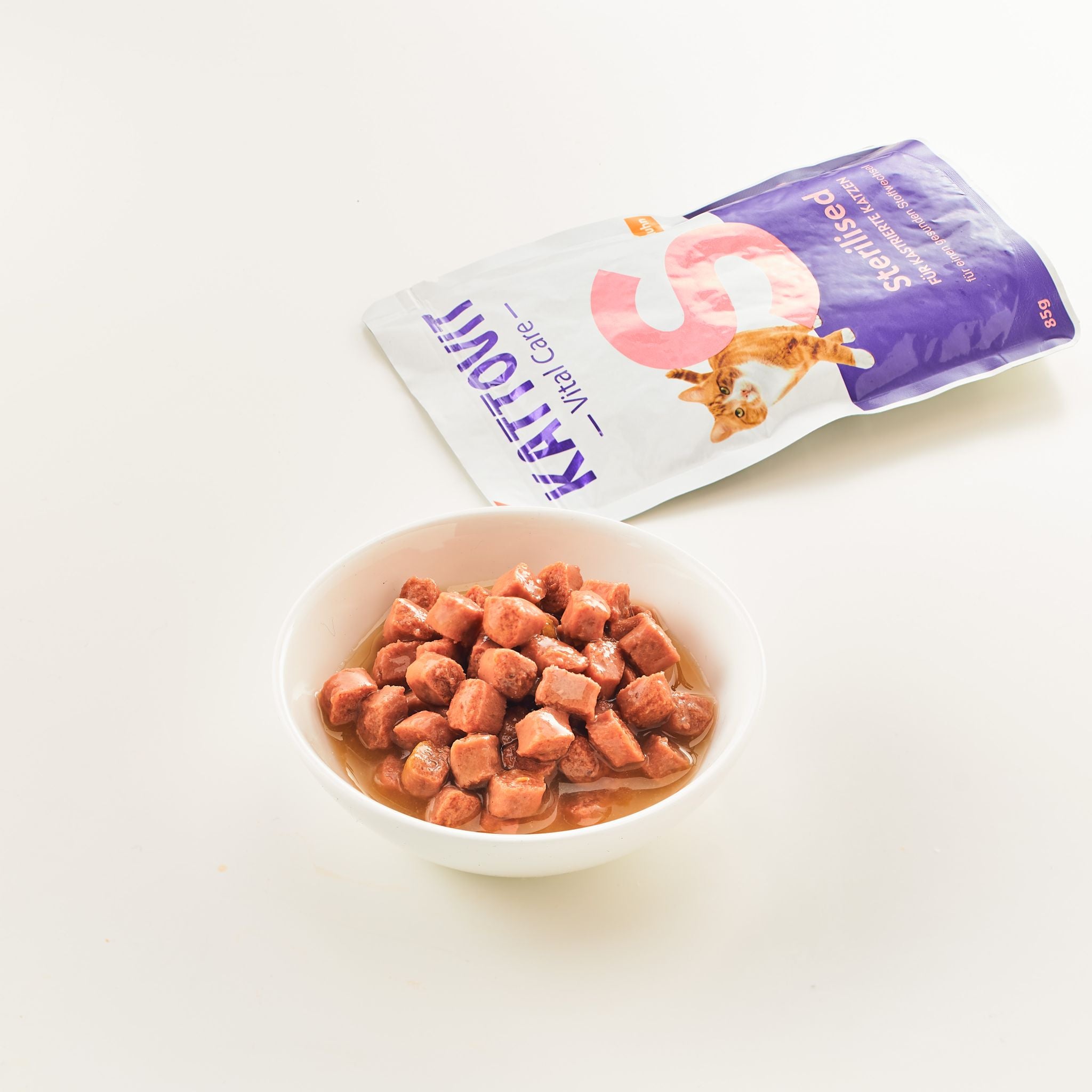 Eine kleine weiße Schüssel mit gewürfelten Fleischstücken in Brühe, daneben eine Verpackung KATTOVIT Sterilised.