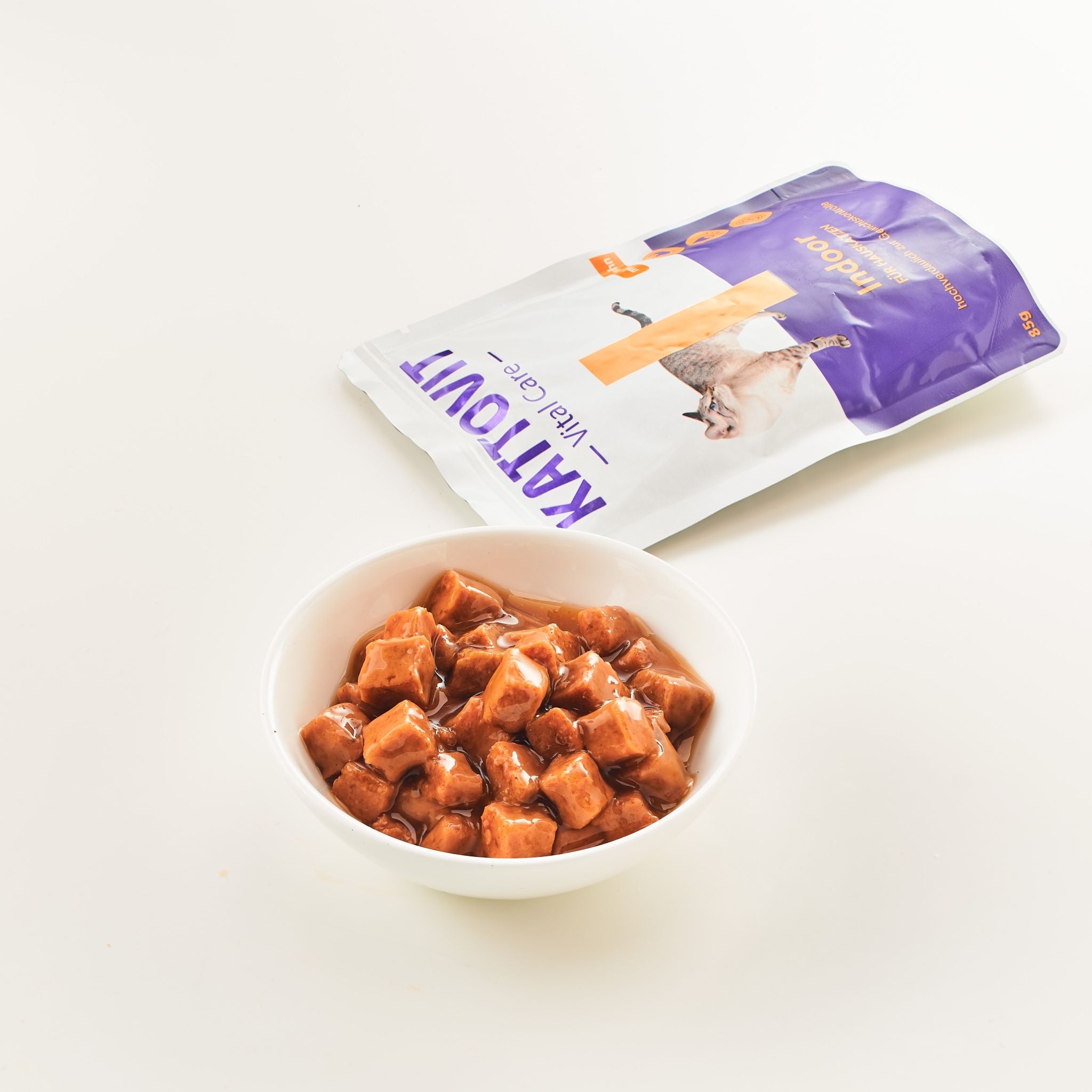 Nassfutterwürfel in Soße mit geöffneter KATTOVIT Verpackung "Indoor" daneben.