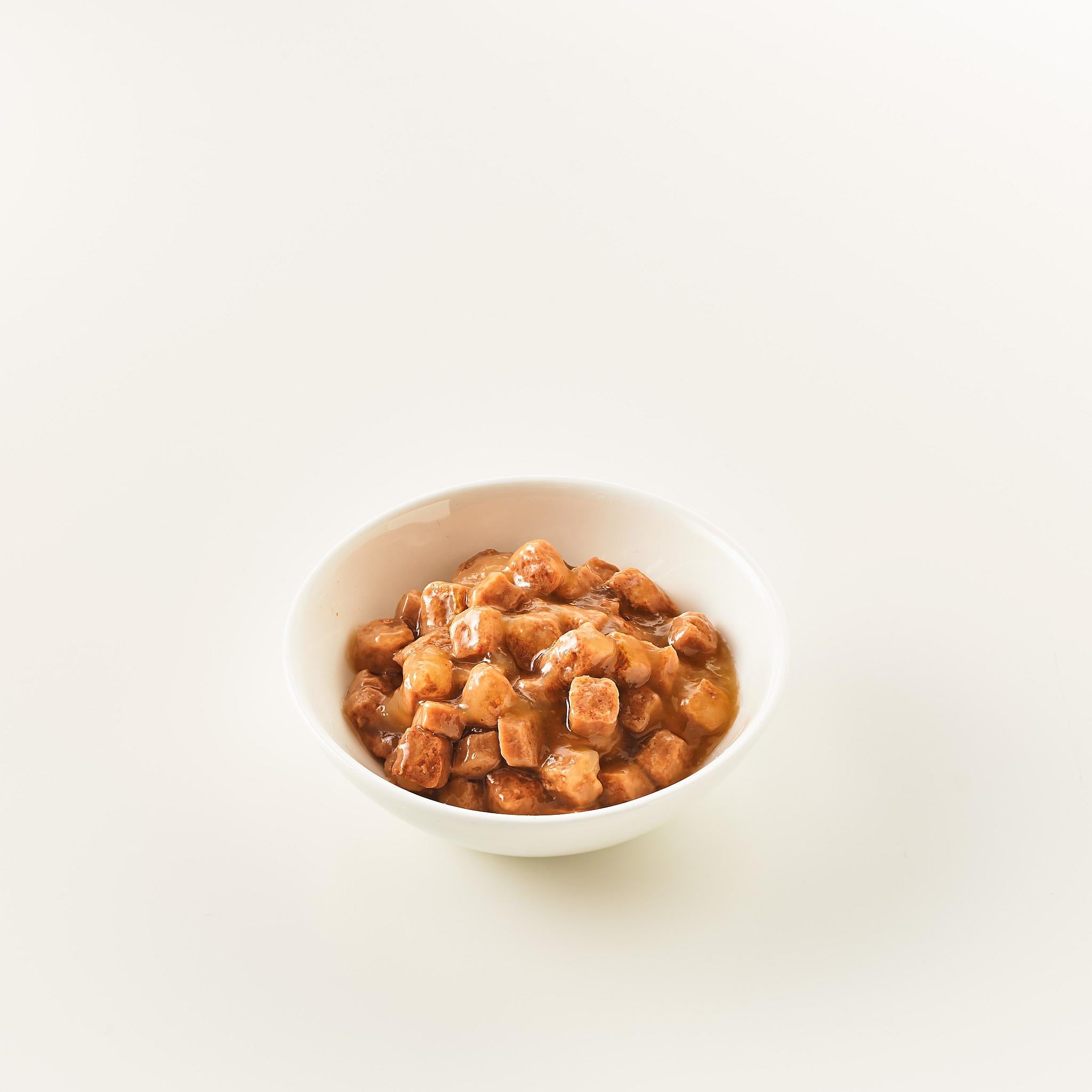 Eine weiße Schüssel, die mit einer braunen, dicken und würzigen Sauce für Katzen gefüllt ist.